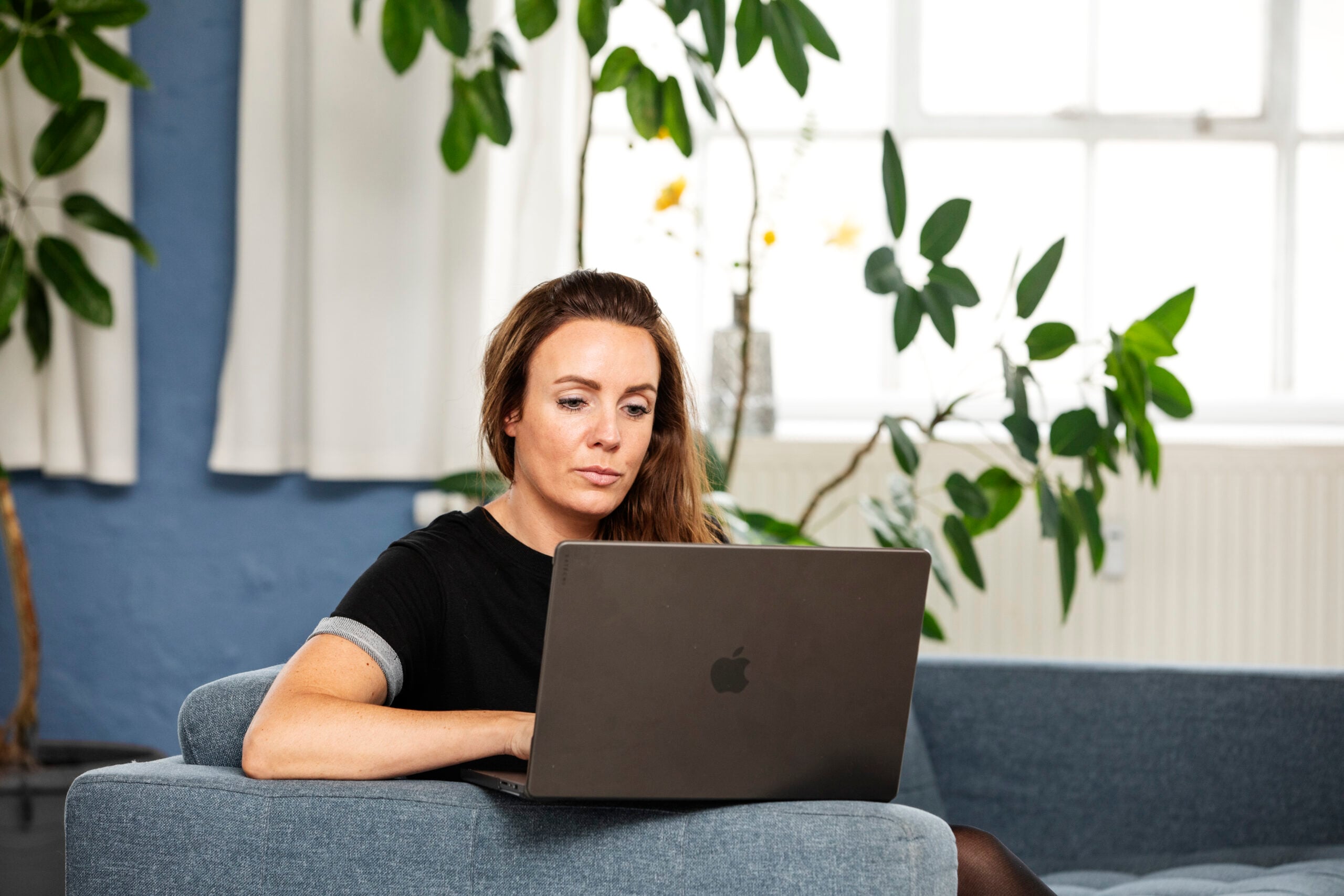 Kvinde der sidder i sofa med en computer