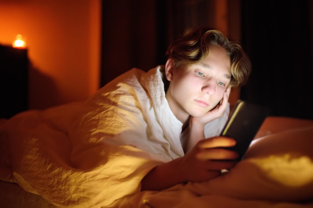 Trist teenage dreng i sengen med sin mobil